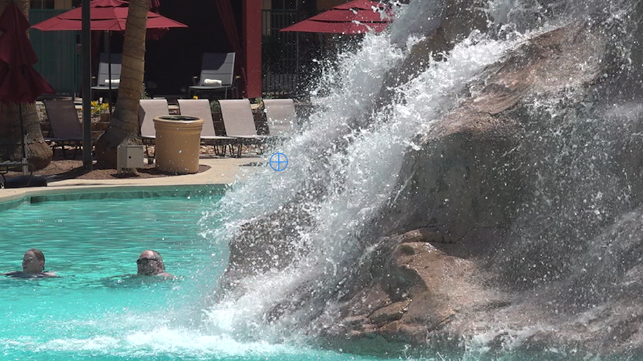 Two people swimming in a pool by a waterfall